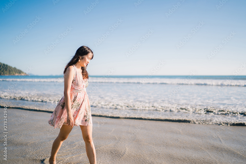 Young Asian woman walking on beach. Beautiful female happy relax walking on beach near sea when sunset in evening. Lifestyle women travel on beach concept. Young Asian woman walking on beach. Beautiful female happy relax walking on beach near sea when sunset in evening. Lifestyle women travel on beach concept.