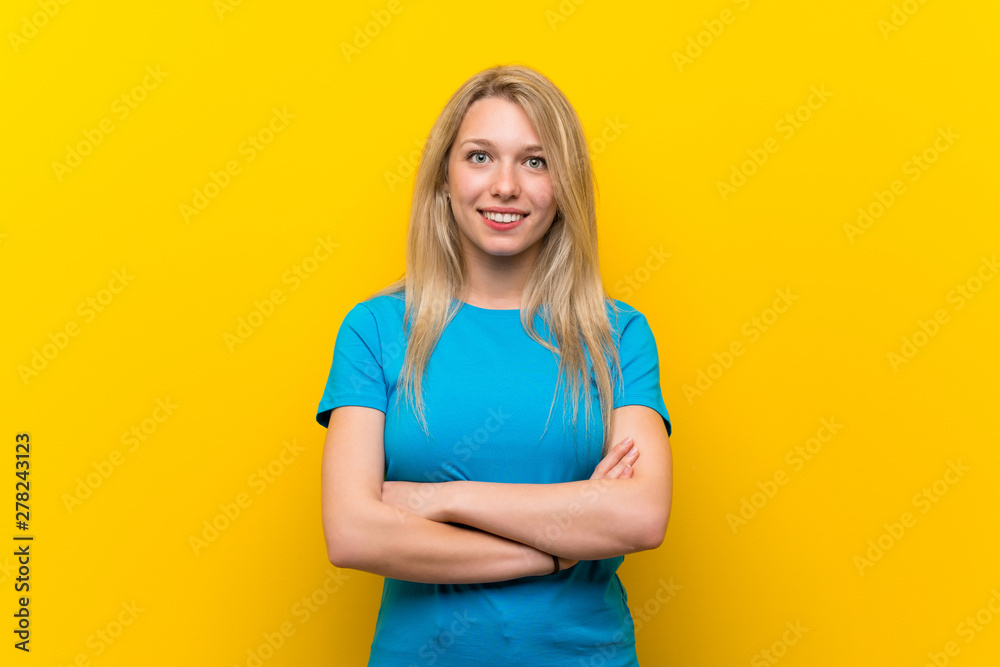 Young blonde woman over isolated yellow background keeping the arms crossed in frontal position Young blonde woman over isolated yellow background keeping the arms crossed in frontal position