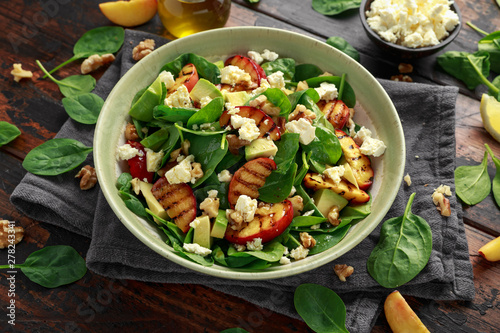 Summer Peach Salad with spinach, avocado, walnuts and feta cheese in rustic bowl. healthy food.