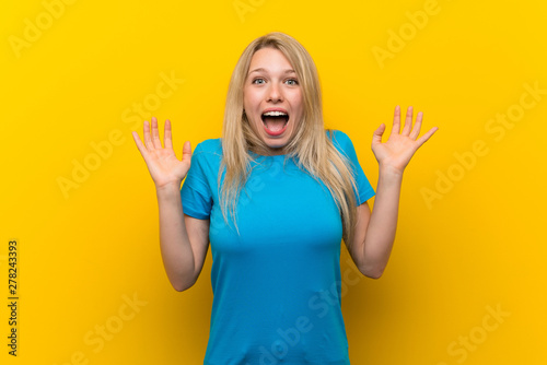 Young blonde woman over isolated yellow background with shocked facial expression