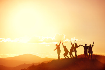 Happy friends or big family's silhouettes at sunset mountains
