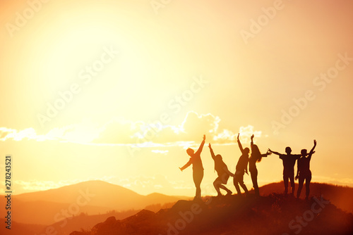 Happy friends or big family's silhouettes at sunset mountains