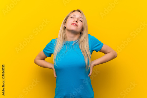 Young blonde woman over isolated yellow background suffering from backache for having made an effort