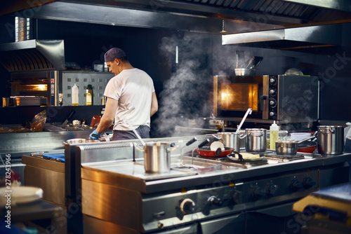 cook stands with his back, Cooking in a modern kitchen, in a restaurant. low key. Copy space for text