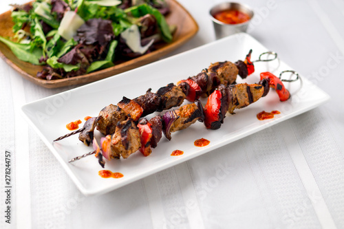 Two pork kebab brochettes in a white plate. These delicious pork meat souvlaki were roasted on the bbq until well-grilled. Cooking food on skewers has been common in many cuisines since ancient times. photo