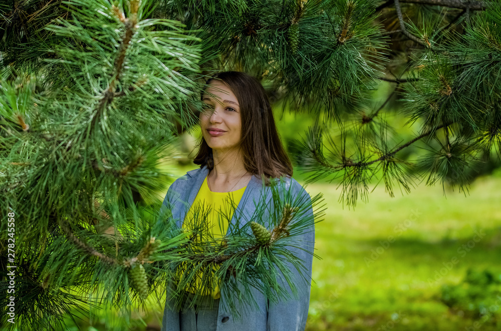 The young woman in gray business suit, in trousers among big green pines in the park. Fashion and style. Portrait. The young woman in gray business suit, in trousers among big green pines in the park. Fashion and style. Portrait.