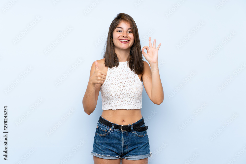 Young woman over isolated blue background showing ok sign and thumb up gesture Young woman over isolated blue background showing ok sign and thumb up gesture