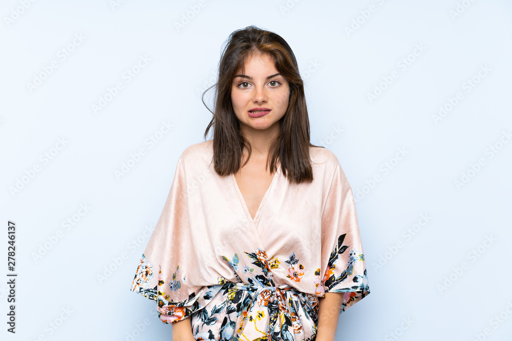Caucasian girl with kimono over isolated blue background having doubts and with confuse face expression Caucasian girl with kimono over isolated blue background having doubts and with confuse face expression