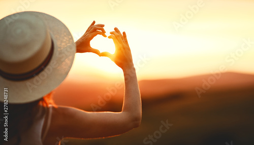 Happy woman with palms of your fingers in shape of a heart on sunset in nature .
