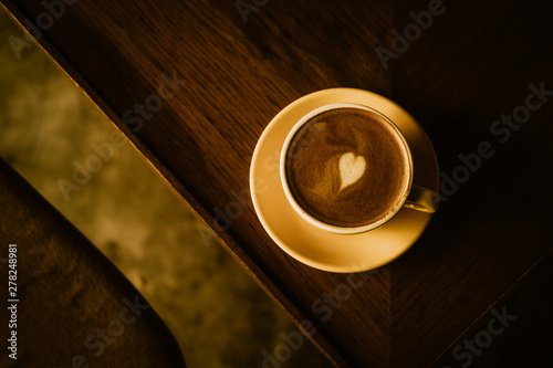 Cappuccino coffee with heart in yellow cup and plate from above. Warm toned filter effect. 
