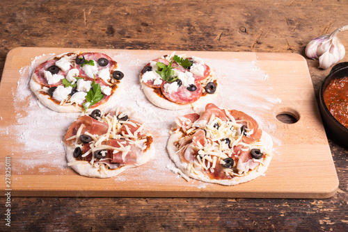 Cooking traditional Italian mini pizza, pizzetta - mini pizza with tomato sauce, salami, jamon and mozzarella cheese on the kitchen blackboard floured