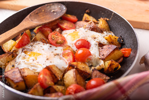 Traditional rural simple dish - fried potatoes with eggs and cherry tomatoes in a pan closeup photo