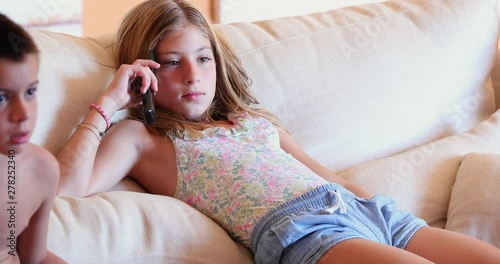 Little girl seated at sofa holding remote control watching TV photo