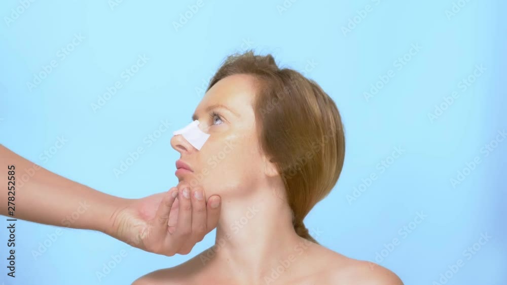 The concept of plastic surgery. rhinoplasty. The hands of the doctor hold the woman's face with a bandage on the nose after the rhinoplasty procedure. on blue background The concept of plastic surgery. rhinoplasty. The hands of the doctor hold the woman's face with a bandage on the nose after the rhinoplasty procedure. on blue background