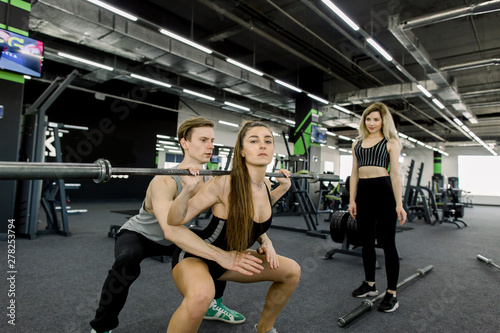 Fit young people lifting barbells over their heads looking focused, working out in a gym with other people
