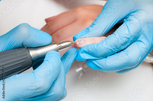 Woman use electric nail file drill in beauty salon. Perfect nails manicure process or operation in close up.