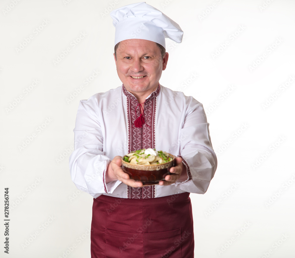 Chef keeps tasty dumplings in his hands. Cook man in slavic national clothes: cap, apron and embroidered.