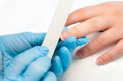 Closeup shot of a woman in a nail salon receiving a manicure by a beautician with nail file. Woman getting nail manicure. Beautician file nails to a customer. © Yauhen