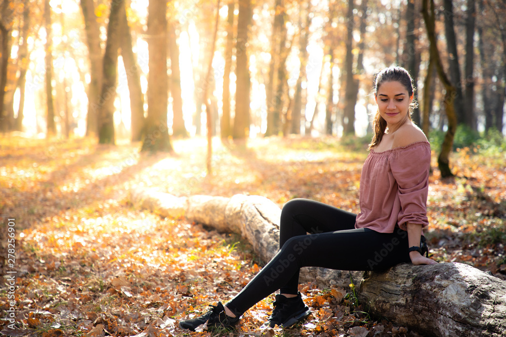 Beautiful girl siting on a trunk with orange foliage and golden sunlight Beautiful girl siting on a trunk with orange foliage and golden sunlight
