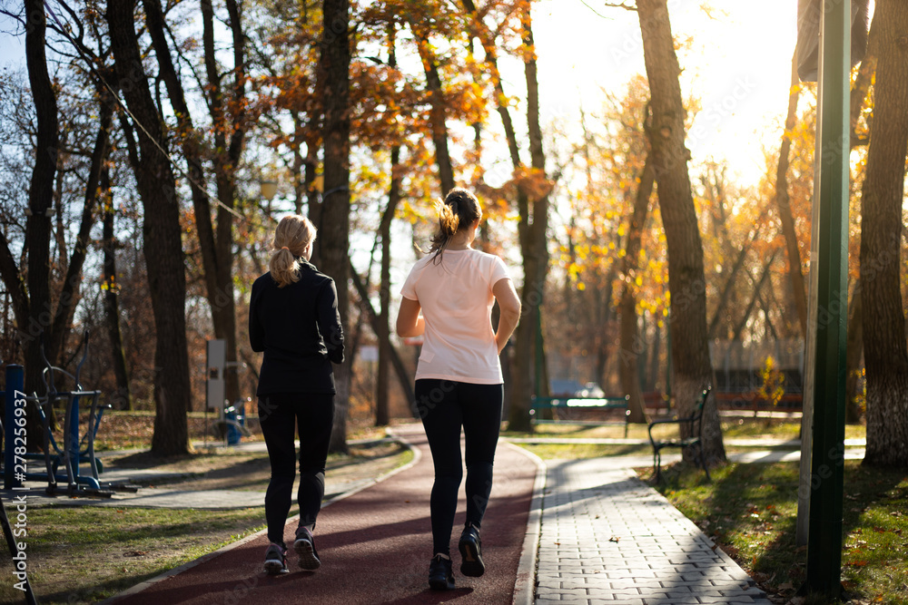 Obraz premium Two beautiful fit women running in parks during fall and suns