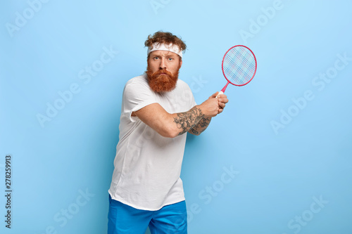 Obraz na plátně Determined serious tennis player beginner holds racket, ready to kick ball, wears casual clothes, spends free time on court, prepares for sport competition, has aim to win match