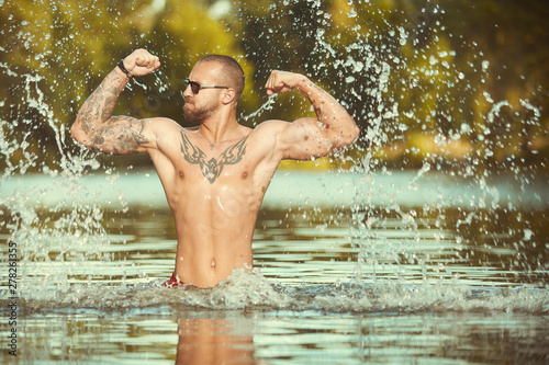 Muscle tattooed man execising in summe city lake water