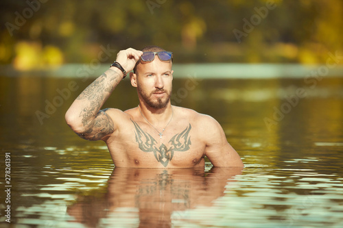 Muscle tattooed man execising in summe city lake water