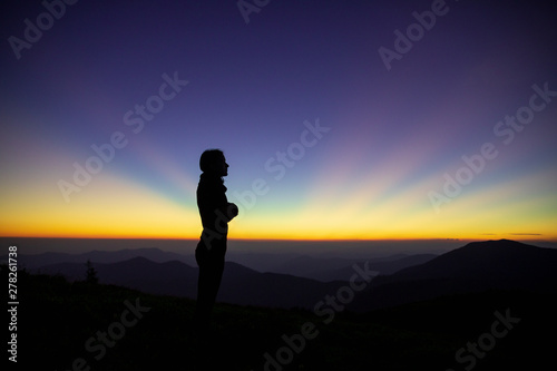 Woman silhouette. Happy traveler standing on top of a mountain and enjoying sunset view. Girl on the background of mountain peaks. Woman hiking in mountains © Serhii