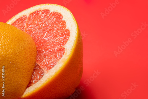 Grapefruit cut in half on vivid red background, copy space. Fruitarianism, vegetarian or vegan food: close-up view of fresh and ripe citrus fruit in bright colors photo