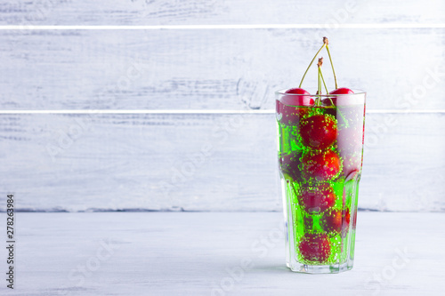 Cherry cocktail. Red cherries in a glass on a white background. Green carbonated drink with sweet cherries. Copy space