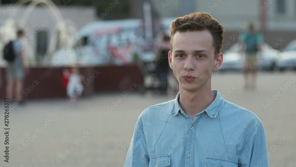 Portrait of young boy in blue shirt with device tasting (smoking) electronic system of heating tobacco on the street Portrait of young boy in blue shirt with device tasting (smoking) electronic system of heating tobacco on the street