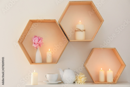 Wooden shelves with beautiful burning candles on light wall