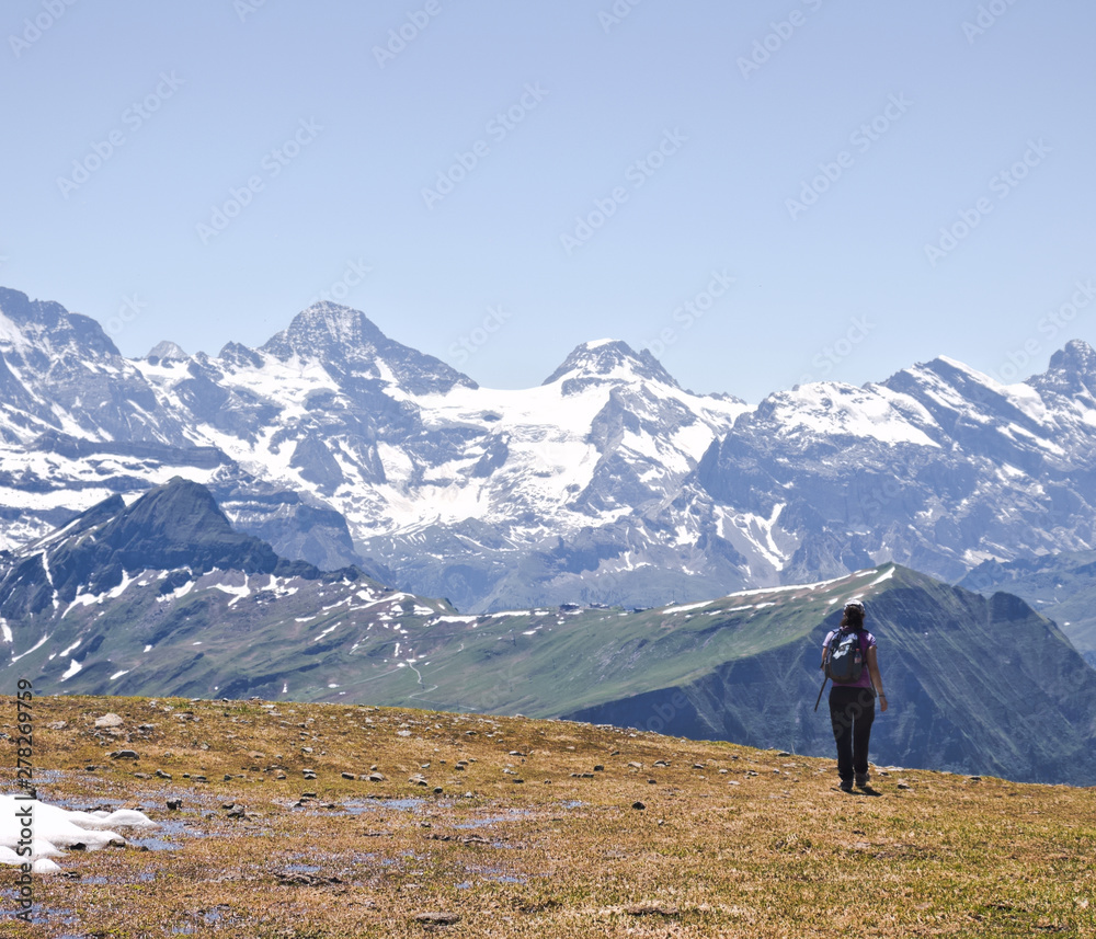 Woman hiker with backpack hiking on plateau with high altitude mountains in the background.