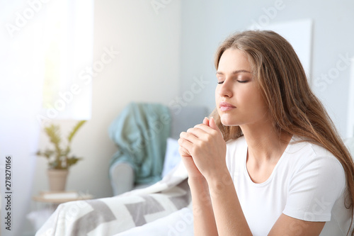 Religious young woman praying to God at home