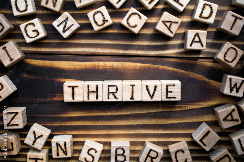 Obraz premium word thrive composed of wooden cubes with letters, to grow, develop, or be successful concept, scattered around the cubes random letters, top view on wooden background