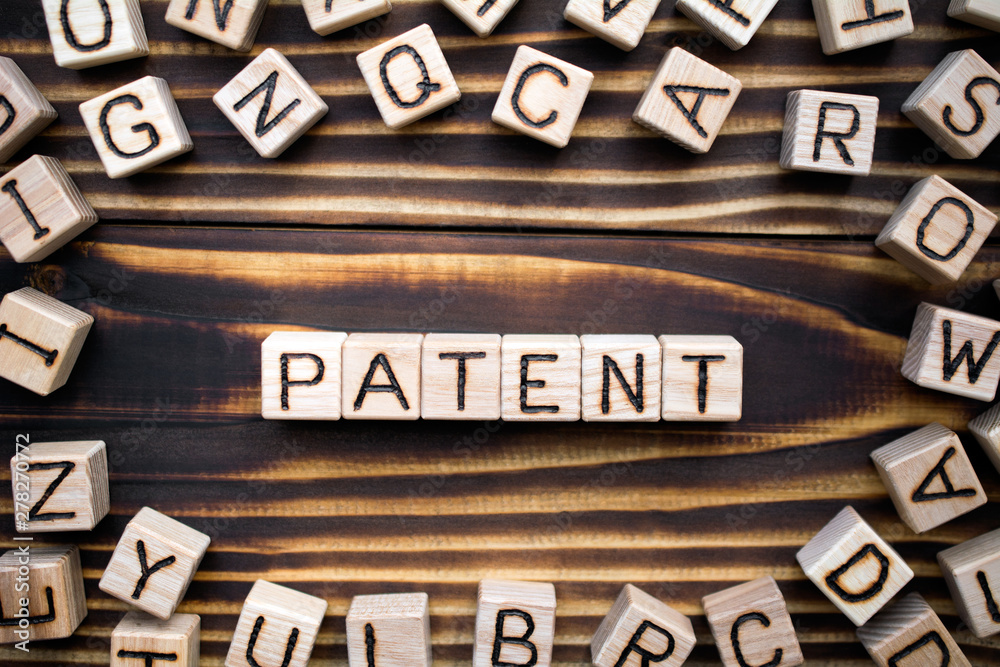 Obraz premium patent composed of wooden cubes with letters, official legal right to make or sell an invention concept, scattered around the cubes random letters, top view on wooden background