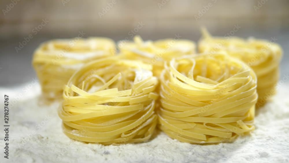 Fettuccine, raw pasta, closeup lie in white flour on a wooden table Fettuccine, raw pasta, closeup lie in white flour on a wooden table