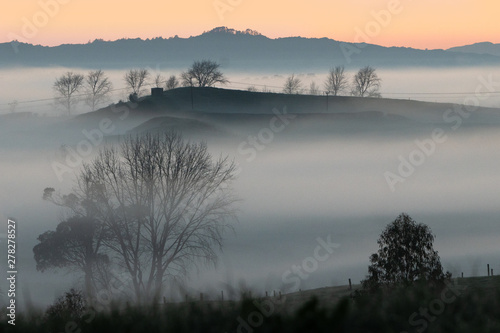 A magical looking sunrise with mist in the valleys and silhouettes of hills and trees. 