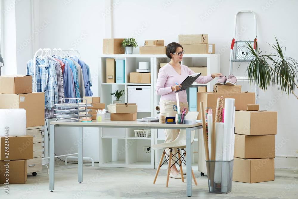 Young manager of online shop taking pair of pink footwear while going to pack them Young manager of online shop taking pair of pink footwear while going to pack them