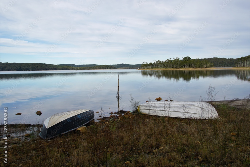Tranquil Lake Scene with two Upturned Wooden Boats on the Shore Tranquil Lake Scene with two Upturned Wooden Boats on the Shore