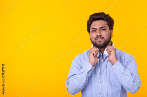Portrait of a positive young indian man with a beard listening to an audiobook on yellow background with copy space. Leisure learning concept.