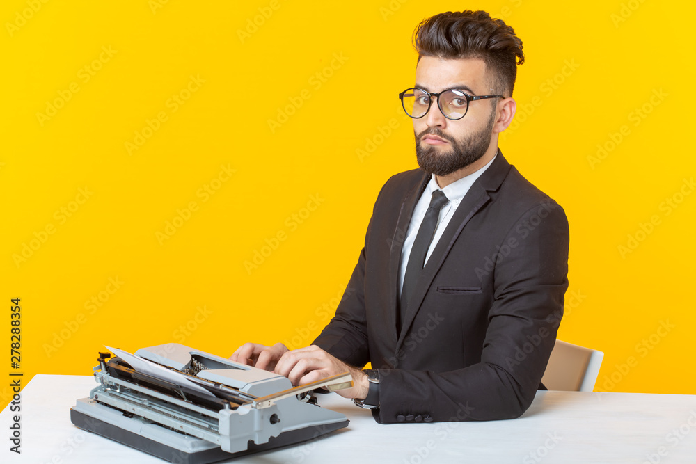 Side view of a young charming male businessman in formal attire and glasses typing on a typewriter text. Concept of business affairs and ideas. Side view of a young charming male businessman in formal attire and glasses typing on a typewriter text. Concept of business affairs and ideas.