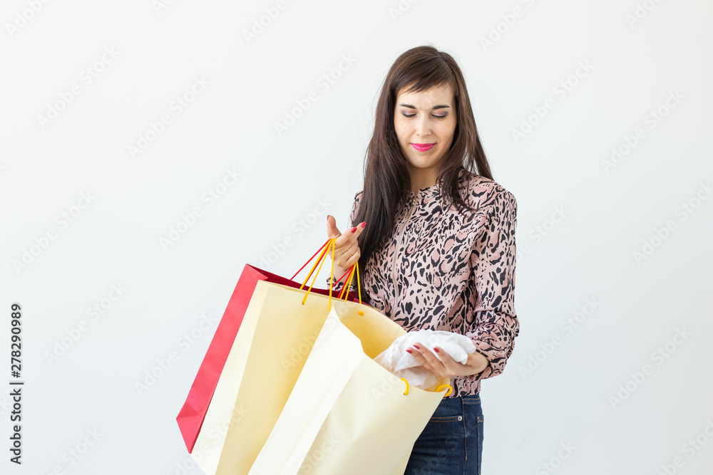 Fototapeta premium Charming young joyful brunette woman holds in her hands bags with a new clothing posing on a white background. Shopping concept.