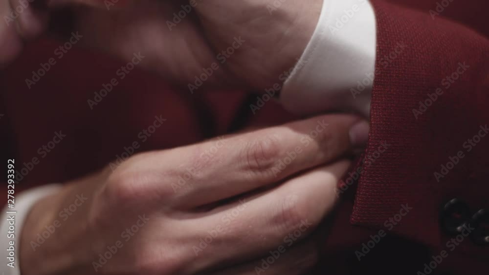 Close up of an elegant man in red suit buttoning shirt sleeve. Flat plane. Low angle shot Close up of an elegant man in red suit buttoning shirt sleeve. Flat plane. Low angle shot
