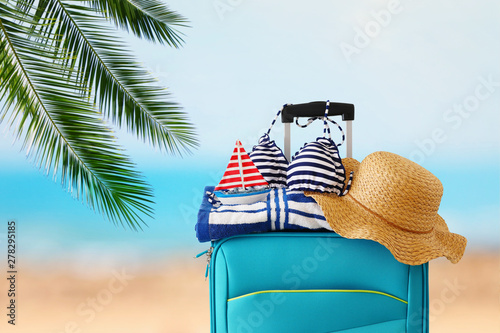 holidays. travel concept. blue suitcase with female hat  bikini  sailing boat and beach towel in front of tropical background