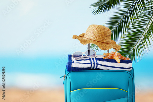 holidays. travel concept. blue suitcase with female hat  starfish  sunglasses and beach towel in front of tropical background