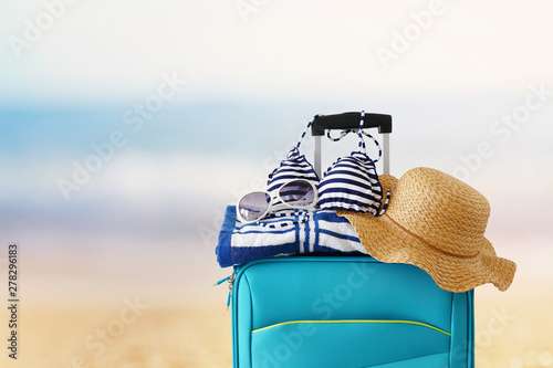 holidays. travel concept. blue suitcase with female hat  sunglasses bikini and beach towel in front of tropical background