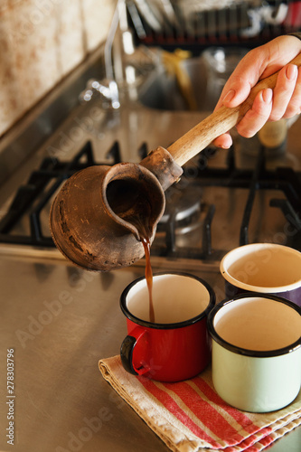 Hand pouring coffee from turk to enamel mugs photo