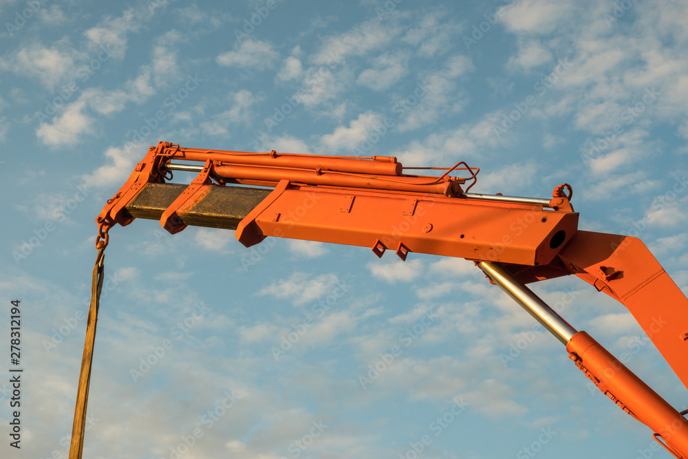 Red crane boom against the blue sky. Car manipulator unloads the pipe. Construction works. Summer. Sunny day. Red crane boom against the blue sky. Car manipulator unloads the pipe. Construction works. Summer. Sunny day.