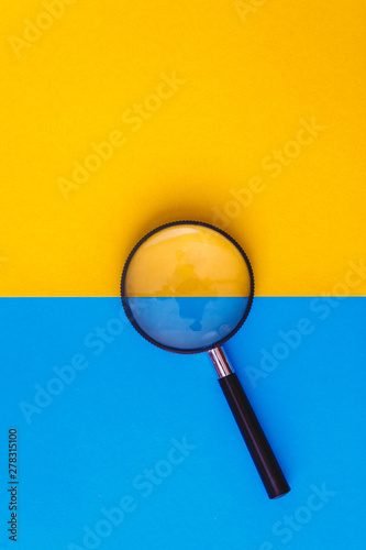 Magnifier lies on yellow and blue background. View from above. Flat lay. Copy space